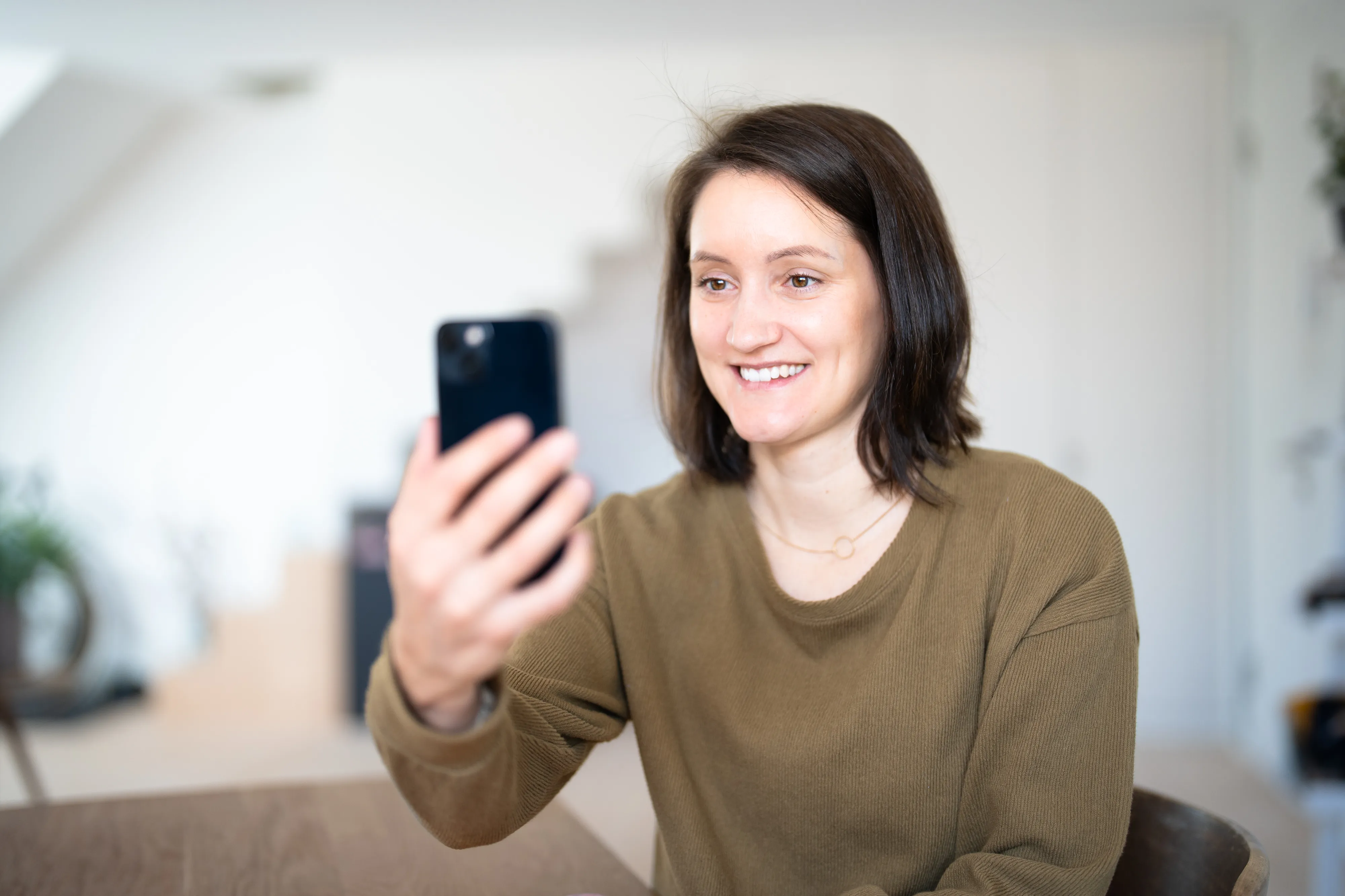 Eine Frau lächelt während sie ein Mobiltelefon vor ihr Gesicht hält